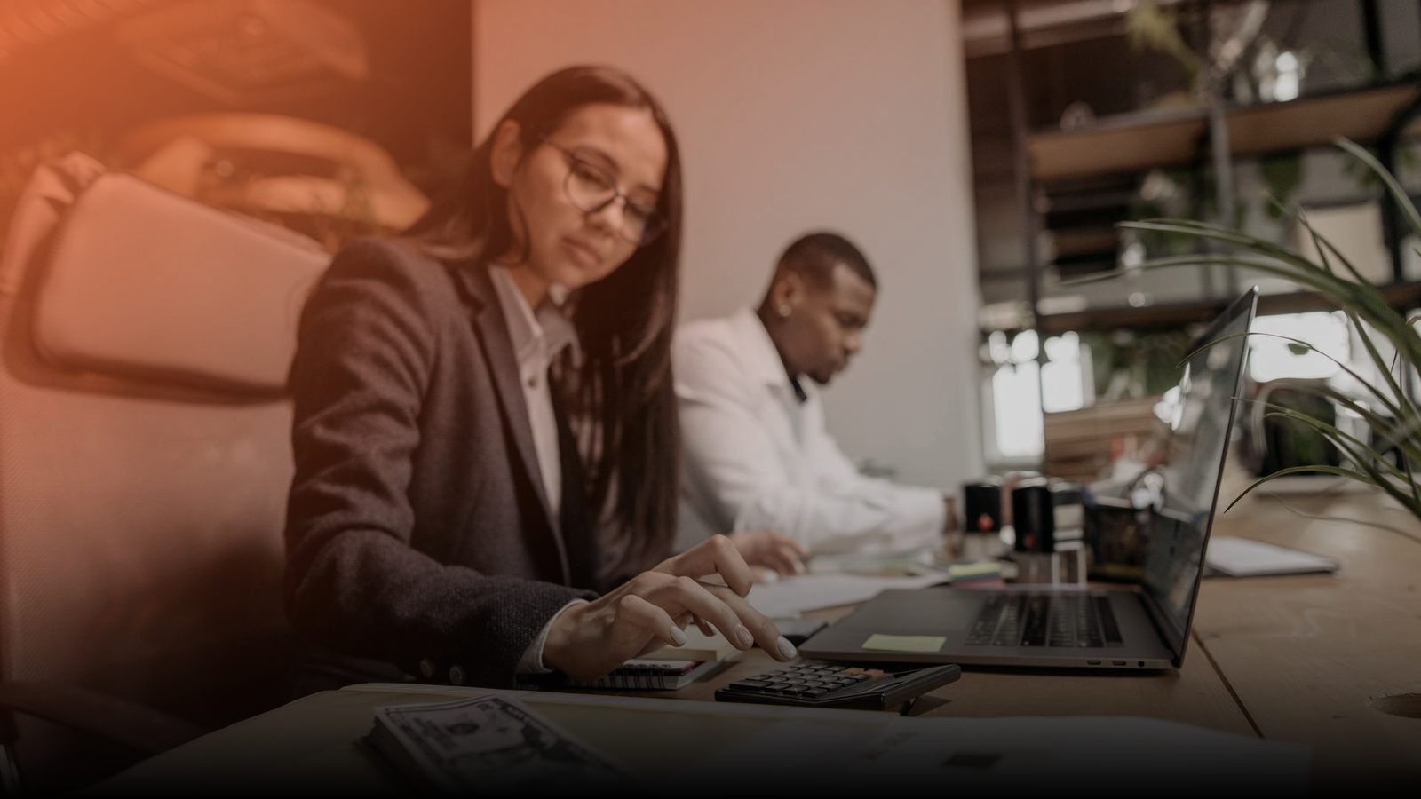 Two accountants working at a desk with a laptop and papers