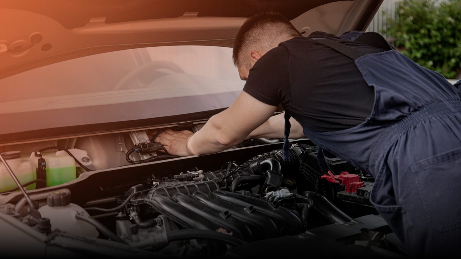 A mechanic working under the open hood of a car