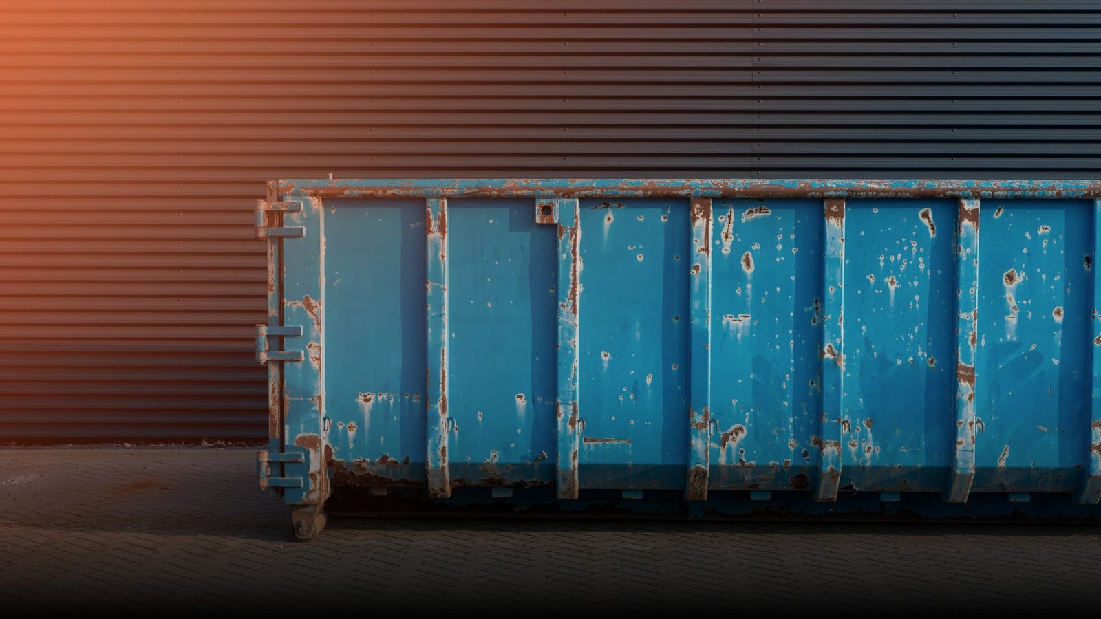A blue dumpster standing in front of a dark building