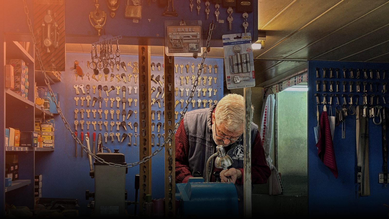 A locksmith at the bench of a key shop, cutting a key under the lamp