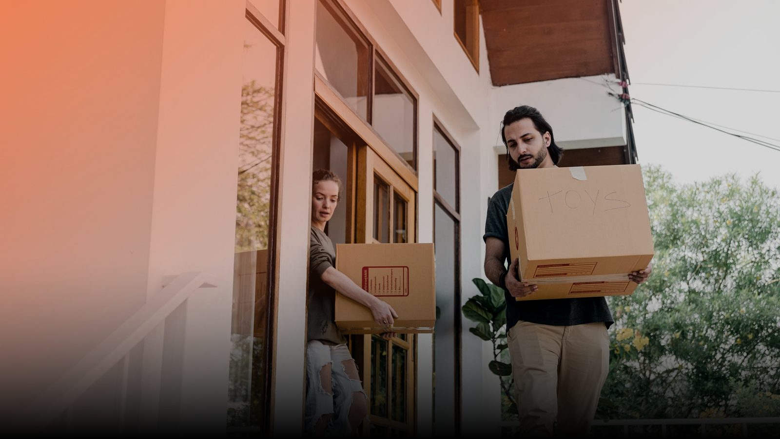 Movers carrying boxes out through the front door of a house