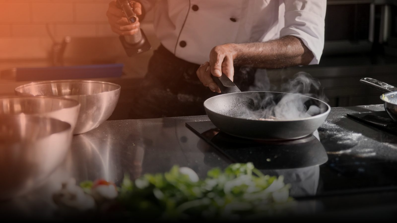 A chef searing food in a pan in a restaurant kitchen