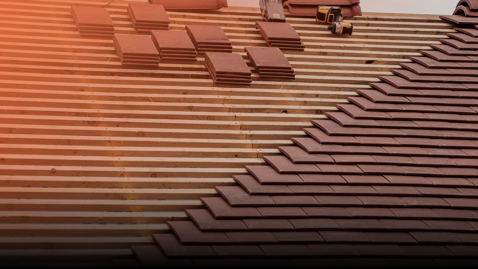 A roofer laying clay tiles on a pitched roof under a grey sky